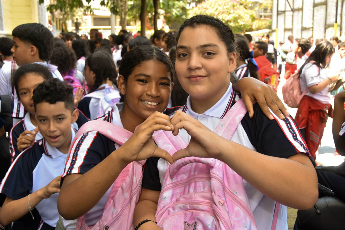 Imagen de dos estudiantes de colegio haciendo un corazón con sus manos