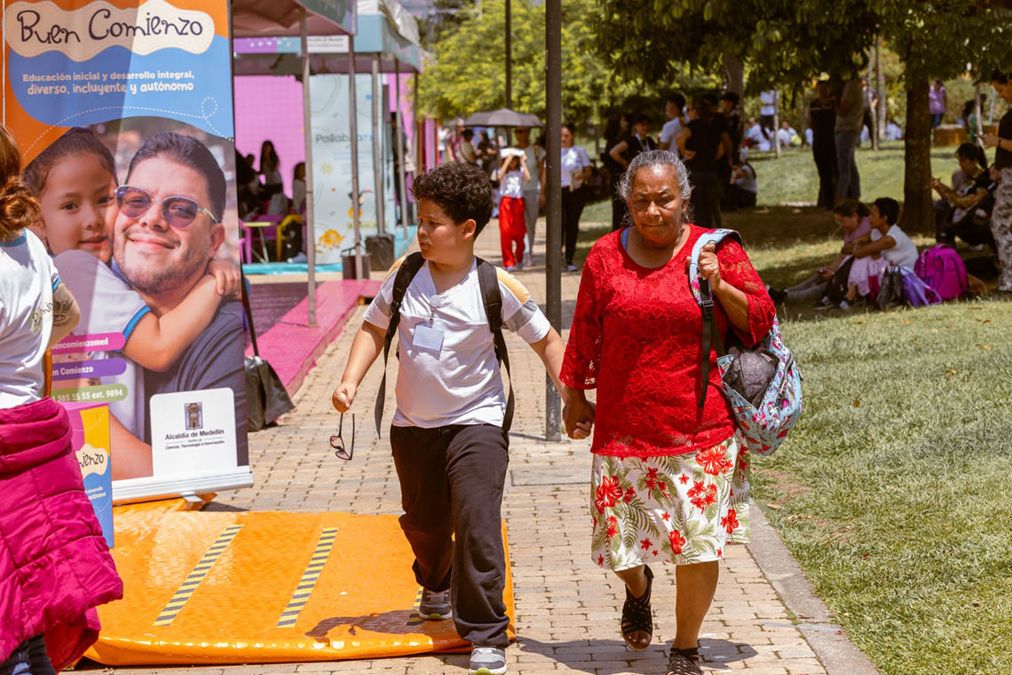 Imagen de adulta mayor tomada de la mano con niño en evento del libro