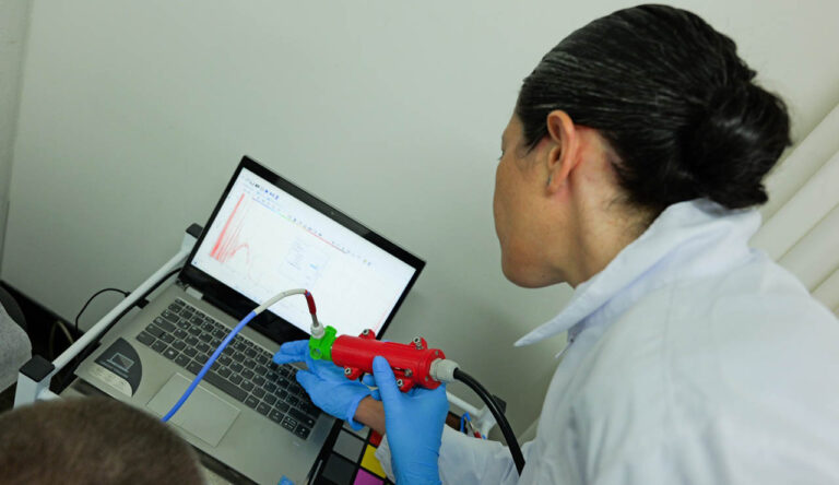 Imagen de personal de la salud con dispositivo en la mano leyendo datos en un computador