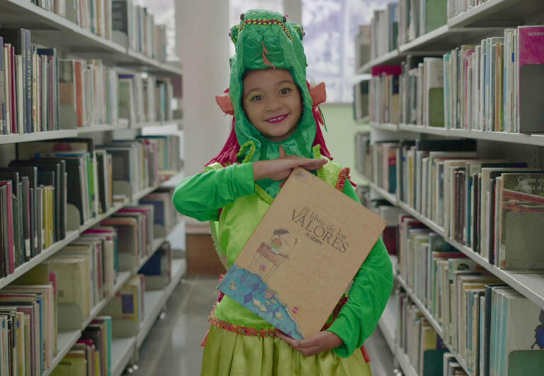 Imagen de niña disfrazada cargando un libreo en una biblioteca