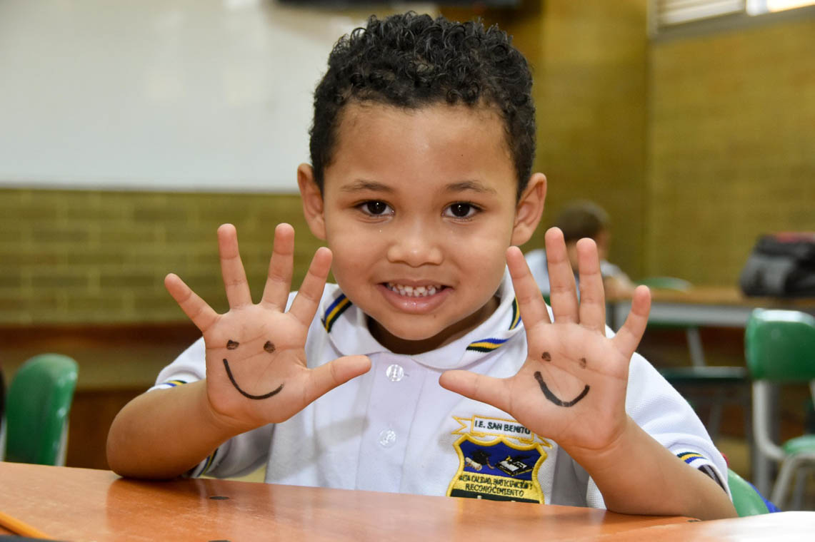 Imagen de un niño sonriente con manitas pintadas con caritas